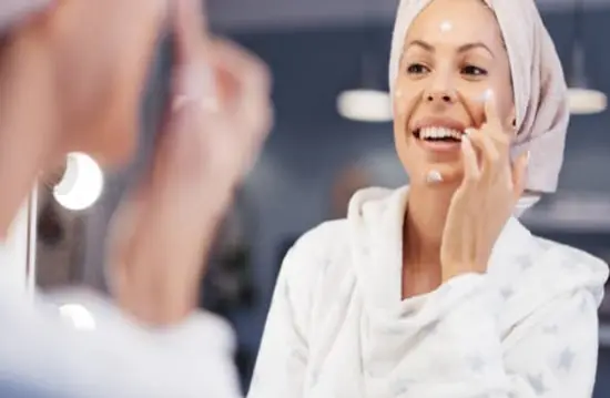 A mature lady applying small amounts of face cream around her face