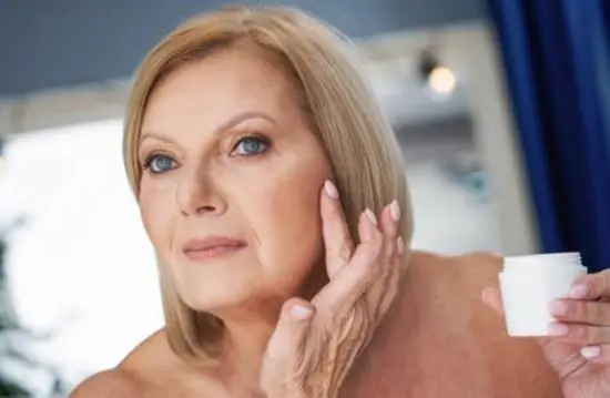 A mature woman applying face crea to her left cheek