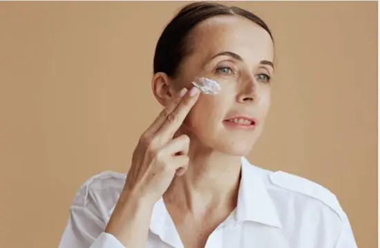 A woman applying eye cream below her right eye lid