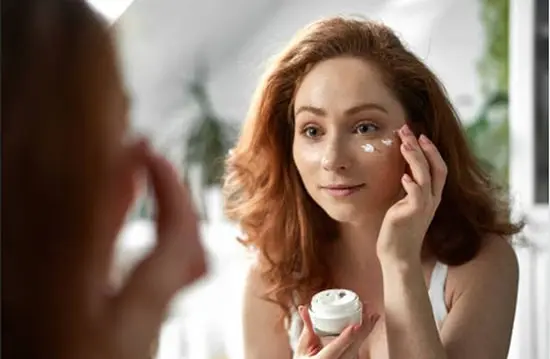 A pretty lady gently rubbing in organic face cream around her face cheeks