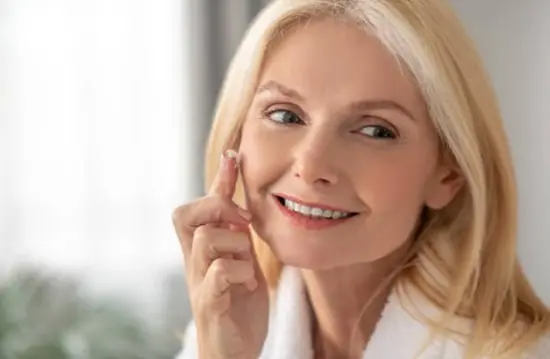 A smiling woman dabbing in face cream around one of her cheeks