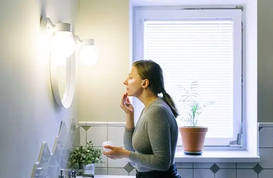 woman applying anti aging cream while looking in the mirror